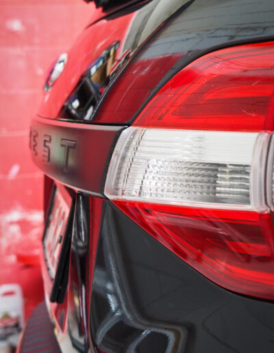 Rear door edge and badge with reflections on paint surface.